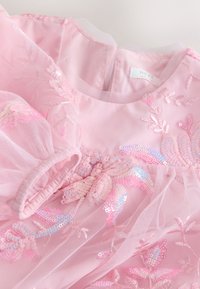 Robe rose avec manches bouffantes transparentes et broderie florale en sequins sur tulle, dotée d'un col rond et d'une fermeture éclair.
