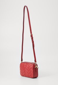 Red quilted crossbody bag in synthetic material with a structured rectangular shape, adjustable strap, and gold-tone zipper hardware.