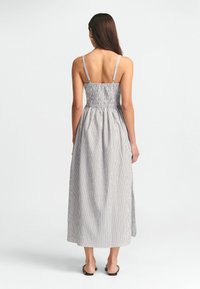 Dryžuota maxi suknelė su plonomis petnešėlėmis, smulkinta liemene ir laisvu sijonu, mėlynos ir baltos spalvų tonais. Lygus audinys su švelnia tekstūra.