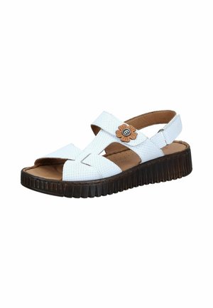 White perforated leather sandal with thick black sole, adjustable straps, and a small brown flower decoration near the ankle strap.