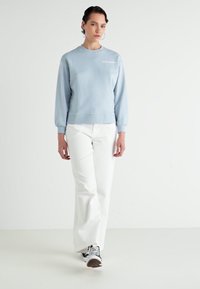 Lichtblauwe sweatshirt met een ronde hals en elastische manchetten, gecombineerd met witte wijde broek en zwart-witte sneakers.