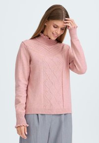 Pull en tricot rose avec un col montant, présentant un motif en losanges à l'avant et des poignets volantés. Texture douce et coupe décontractée.
