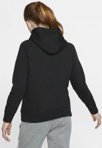 Črna kapuca s sweatshirtom gladke teksture, prilegajoče zasnove in rebrastimi manšetami, v kombinaciji z sivimi hlačami za sproščen videz.