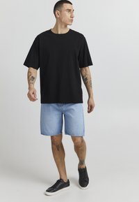 T-shirt nera a maniche corte, pantaloni denim azzurri e scarpe da ginnastica nere; outfit casual con una vestibilità rilassata e design minimale.
