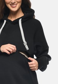 Felpa nera con cappuccio, coulisse e dettagli con zipper frontale. Tessuto comodo, vestibilità ampia, dotata di tasca a marsupio e una morbida fodera interna.