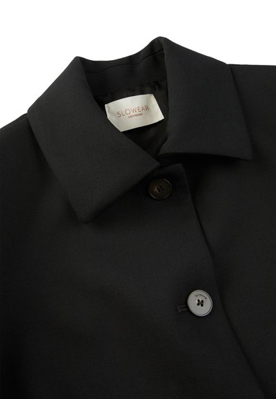 Cappotto nero con collo strutturato, tessuto liscio e un solo bottone con logo. L'etichetta interna recita "SLOWEAR MONTEGRO."