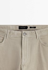 Pantalon beige en velours côtelé à coupe fuselée avec poches avant, passants de ceinture, fermeture à bouton et étiquettes de marque internes à la taille.