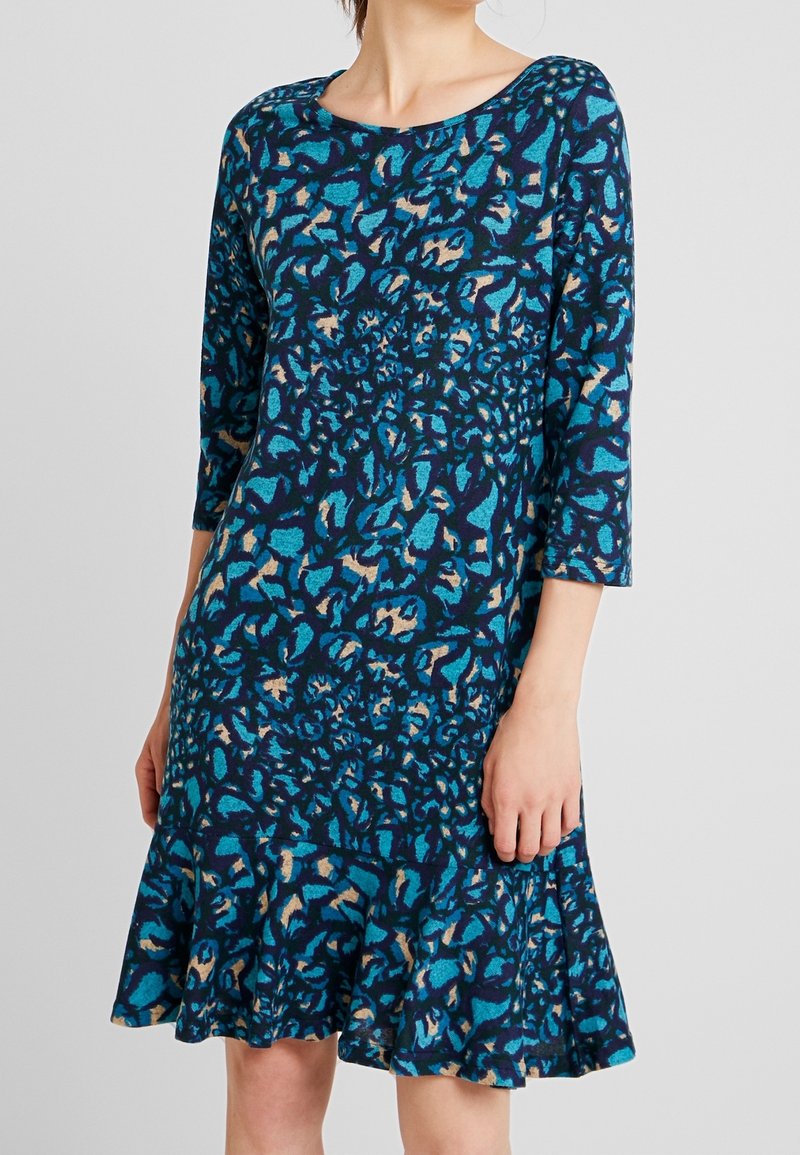 Knälång klänning i blått och svart med ett abstrakt mönster. Har trekvartslånga ärmar och en utsvängd nederkant för en avslappnad passform.