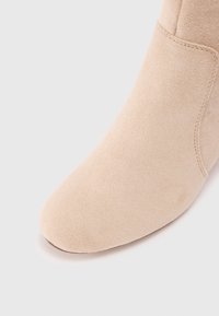 Beige nubuk bőr bokacipő kerek orral és sima textúrával. Az oldalán varrott díszítések találhatók, amelyek fokozzák a dizájnt.