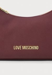 Marokas krāsas Love Moschino somiņa ar zelta rāvējslēdzēju un zelta metāla logo centrā priekšpusē.