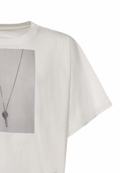 T-shirt à manches courtes couleur ivoire avec une photo imprimée d'une clé argentée sur une fine chaîne, affichée au centre avant.