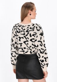 Cremefarvet sweater med sort abstrakt leopardprint, ribbestrikket krave og manchetter, parret med en sort læder mini-skirt. Blød tekstur og afslappet pasform.