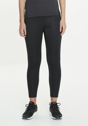 Zwarte sportleggings van rekbare stof, met een slim fit en subtiele zijknoppen, gecombineerd met zwarte sportschoenen.