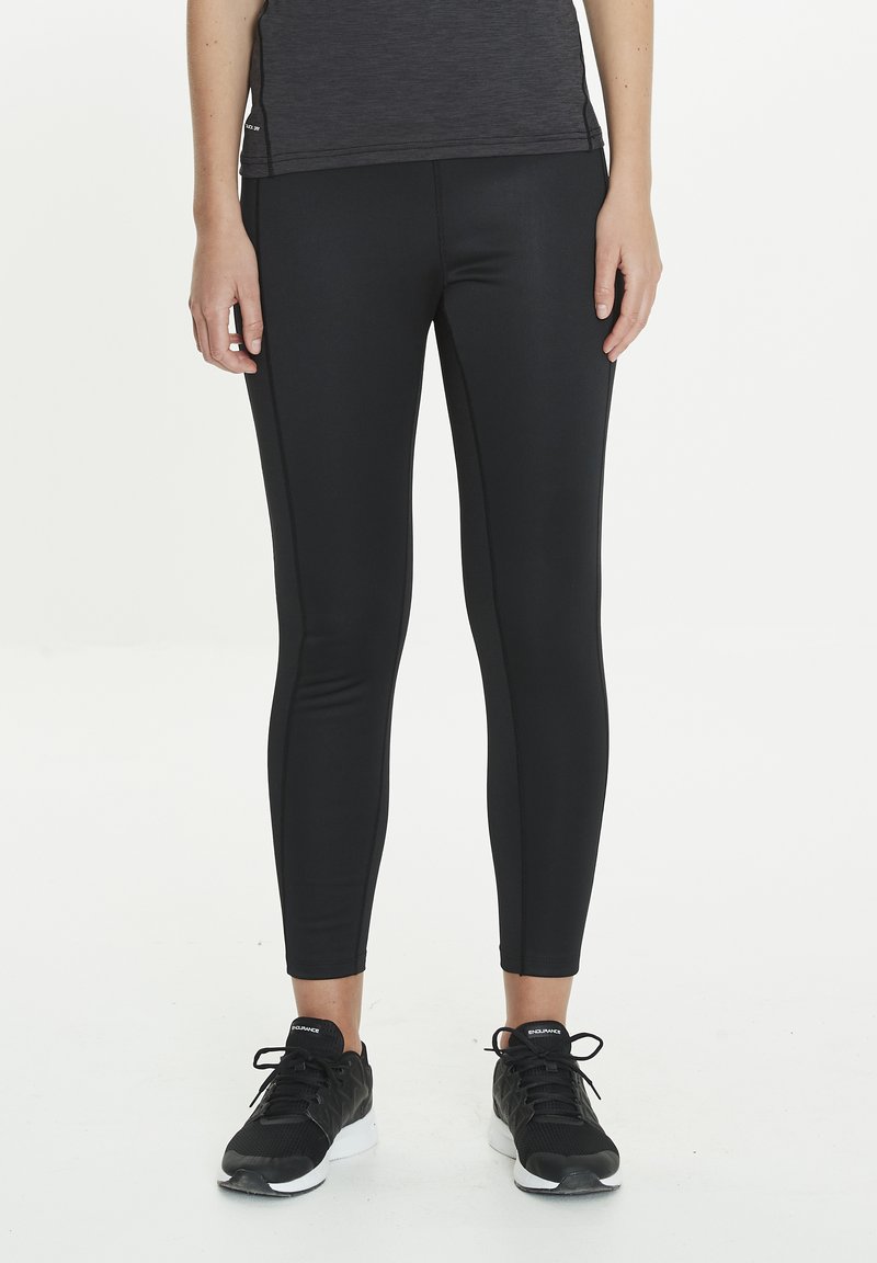 Leggings de sport noirs en tissu extensible, avec une coupe slim et des coutures latérales discrètes, assortis à des chaussures de sport noires.