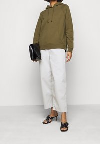 Olijfgroene hoodie met een voorkantzak, gecombineerd met witte wijde broek en zwarte gehakte sandalen met een knoopontwerp.