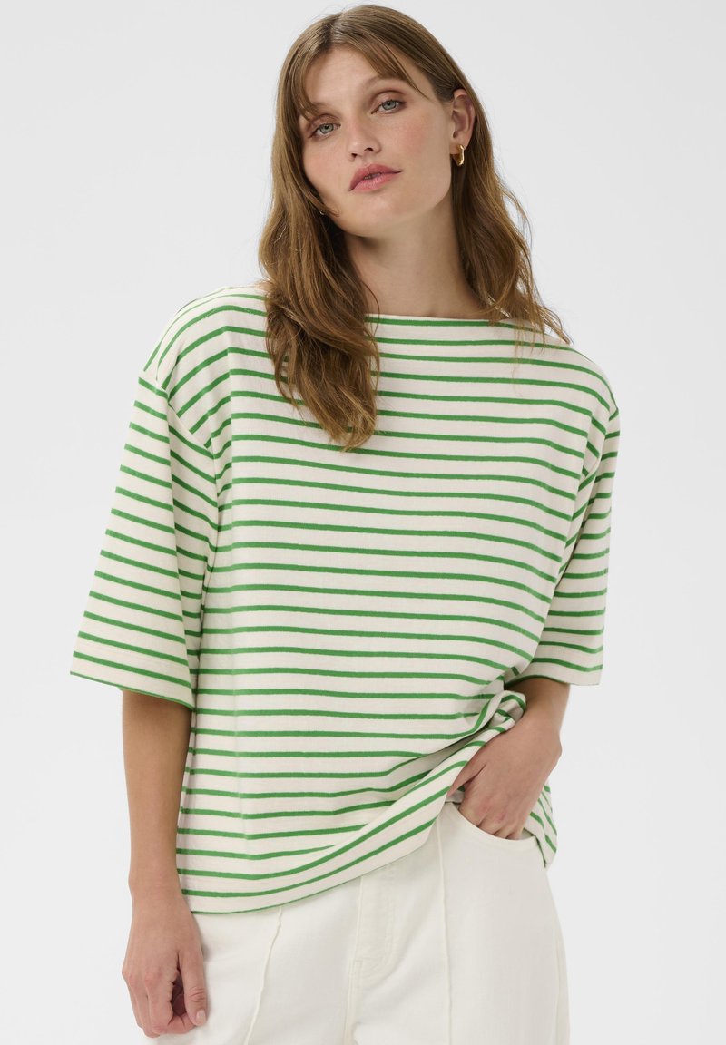 Chemise à manches courtes rayée vert et blanc en tissu doux, avec un large décolleté et une coupe décontractée. Portée avec un pantalon clair.