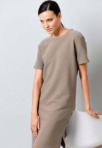 Kurzärmliges braunes Strickkleid mit lockerer Passform, Rundhalsausschnitt und seitlichen Schlitzen. Glatte Textur, minimales Design und knieumspielende Silhouette.