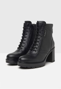Zwarte leren enkellaarsjes met een chunky hak, voorzien van een vetersysteem aan de voorkant en een rits aan de zijkant. Glad materiaal en minimalistischer ontwerp.