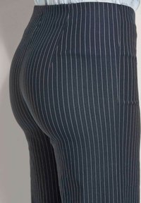 Donkerblauwe pinstriped broek met dunne rode strepen, tapered ontwerp en een gladde textuur. Zijkant benadrukt de pasvorm en taille-detail.