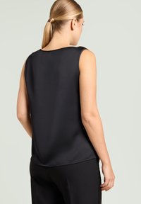 Czarny top bez rękawów o gładkiej fakturze i prostym okrągłym dekolcie, zestawiony z czarnymi spodniami. Charakteryzuje się prostym krojem.