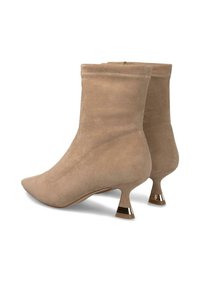 Botas de ante beige hasta el tobillo con puntas afiladas, tacones cortos y acampanados con ribete metálico y cremalleras laterales, mostradas desde ángulos trasero y lateral.