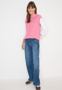 Vaaleanpunainen ribattukangas ilman hihoja oleva toppi yhdistettynä leveälahkeisiin sinisiin farkkuihin ja ruskeisiin lenkkareihin. Asusteessa on rento istuvuus ja epämuodollinen tyyli.