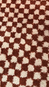 Covor texturat cu un model șah în culori alternante roșu-maronii și albe; fibrele moi și pufoase creează o suprafață primitoare.