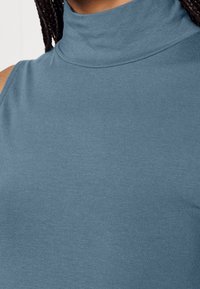 Top senza maniche aderente in morbido tessuto a costine. Presenta un collo alto e una texture liscia in un colore blu tenue.