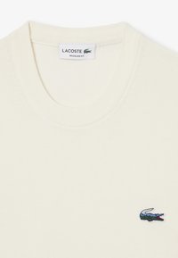 T-shirt in cotone color crema con scollo rotondo, caratterizzato da un piccolo logo di coccodrillo ricamato sul lato sinistro. Design a vestibilità regolare.
