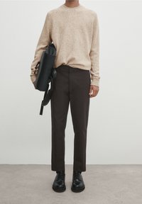 Beige pilkkukuvioinen neule, mustat slim-fit housut, mustat nauhakenkät, pitäen mustaa olkalaukkua, jossa on kahva ja hihna.