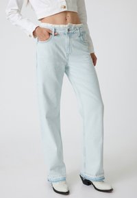 Jeans de mezclilla azul claro con cintura alta y cinturilla elástica. Tienen piernas rectas, un sutil detalle de costura y un ligero desgaste en el dobladillo.