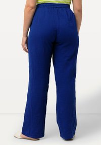 Blå, vida byxor tillverkade av textil med struktur och elastisk midja. Har en avslappnad design som slutar vid ankeln.