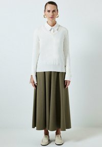 V-kaulusneule valkoisena, oliivinvihreä pitkä hame, valkoiset loaferit. Irtonainen malli, sileä rakenne, pitkät hihat ja kalvosin yksityiskohtia. Kultaiset renkaat korvakoruina.