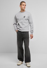 Hall grey kapuutsiga särgiga, millel on must "F" logo rinnal, ribitud varrukatega, koos laia musta teksade ja heledate spordijalanõudega. Sile, hoolitsetud kangas.