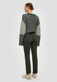 Pull léger à rayures, cropped, en vert foncé et gris clair ; associé à un jean slim vert foncé et des baskets beiges. Texture lisse.