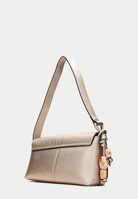 Metalická béžová kožená kabelka se strukturovaným tvarem, hladkým povrchem a krouceným popruhem s ozdobnými korálky na jedné straně.