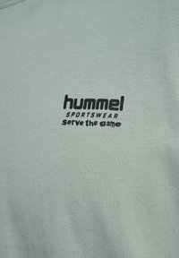 Mintgrön t-shirt i bomull med svart "hummel"-logga och texten "serve the game". Enkel design med rund halsringning.