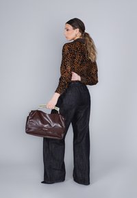 Bruine leren handtas met gouden hardware en glanzende textuur. Draag met een blouse in leopardprint en wijde, donkere spijkerbroeken.