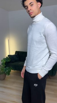 Pull à col roulé blanc à manches longues, porté avec un pantalon jogger noir orné d'un logo. Texture douce, coupe ajustée.