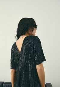 Schwarzes Paillettenkleid mit kurzen Ärmeln, V-Ausschnitt, mit vertikalen Streifenmustern. Glatte Textur und fließende Silhouette.