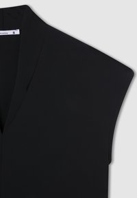 Top senza maniche nero realizzato in un tessuto leggero e liscio. Presenta un collo a V e una struttura delle spalle progettata per un look moderno.