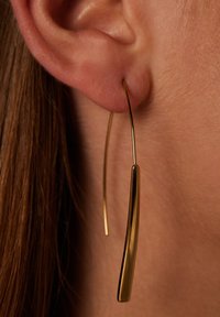 Gouden, langwerpige oorbellen met een slank, gebogen ontwerp. Lichtgewicht, met een gladde afwerking en een minimalistische esthetiek.