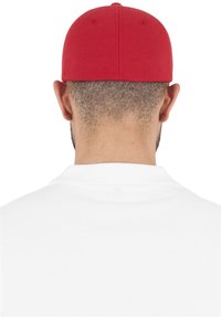 Piros baseball sapka, strukturált formával, szövetből készült, hátulra fordítva viselve egy fehér póló felett. Nincsenek látható logók vagy minták.