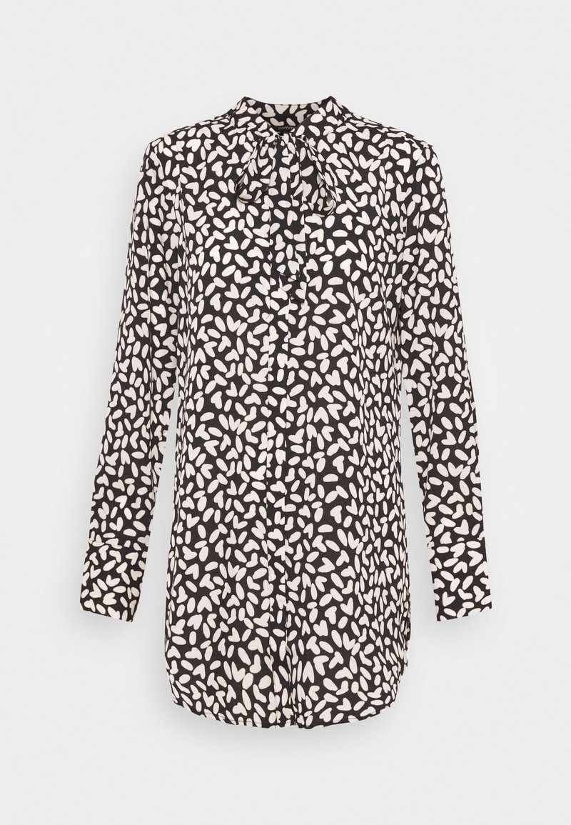 Blouse noire à manches longues avec des taches blanches abstraites en forme de cœur et un détail noué sur le devant, présentée sur un fond uni.