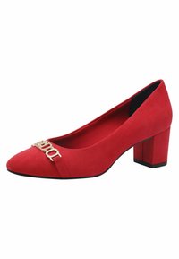 Röda mocka klackpumps med blockklack som har en spetsig tå, en framträdande guldlogo på framsidan och en slät, texturerad yta.