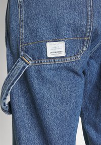 Jeans de mezclilla azul con un bolsillo parche y una etiqueta que dice "URBAN JEANSWEAR JACK & JONES", con detalles de costura visibles.