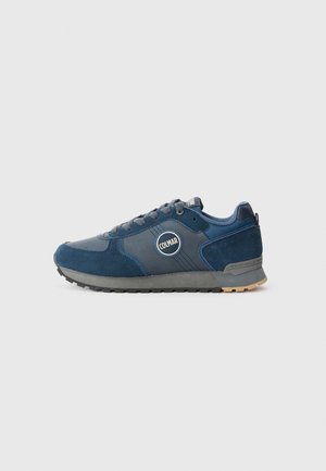 Dunkelblaue Sport-Sneaker mit einer Kombination aus Wildleder und Textilmaterialien, runder Logo-Applikation, strukturiertem Profil und Schnürdesign.