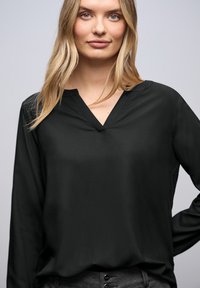 Blusa nera a maniche lunghe con scollatura a V. Realizzata in un tessuto morbido e leggero. Caratterizzata da una vestibilità comoda con dettagli minimi.