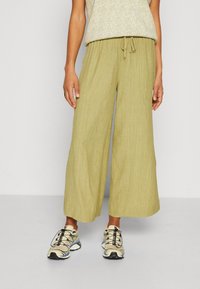 Ljusgröna vida byxor i texturerat tyg, med elastisk midja och snörning. Matchas med beige sneakers.