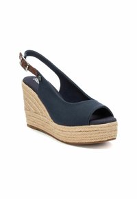 Zapato de cuña de lona marina con puntera abierta, correa ajustable en el tobillo y plataforma de yute trenzado. Presenta una suela tipo espadrille texturizada.